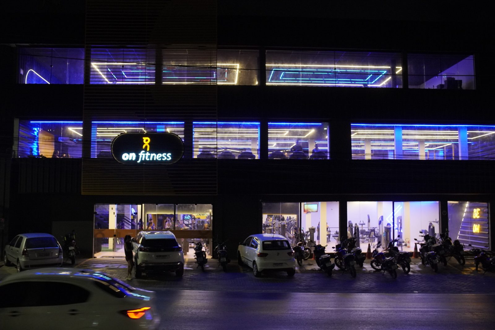 Fachada iluminada da On Fitness Abreu e Lima à noite, com letreiro neon e três andares de academia